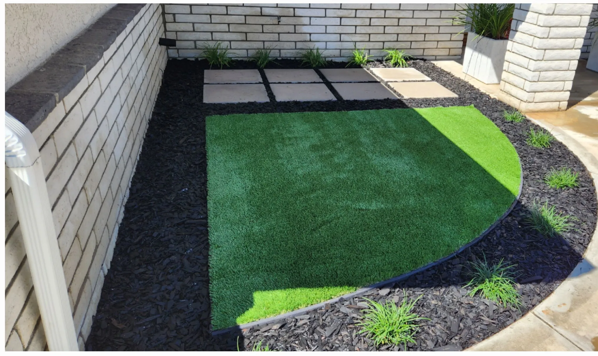 Small side yard with synthetic turf, paver squares, and mulch border