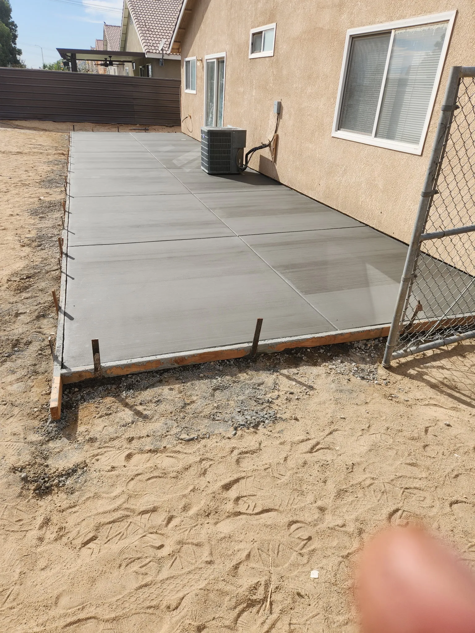 Freshly poured concrete patio slab along the back of a home