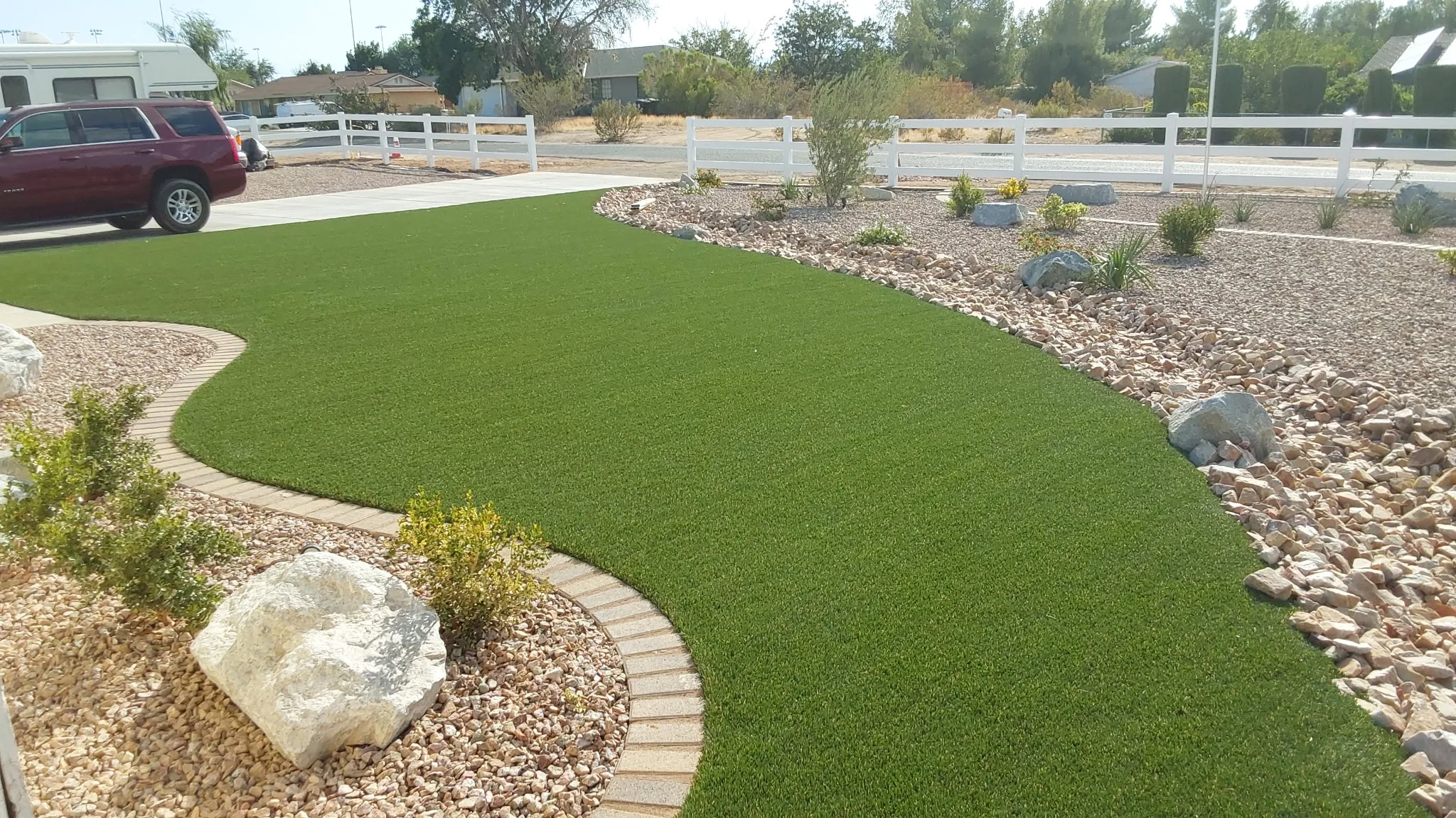 Front yard synthetic turf paired with a decorative rock and boulder bed along a vinyl fence line