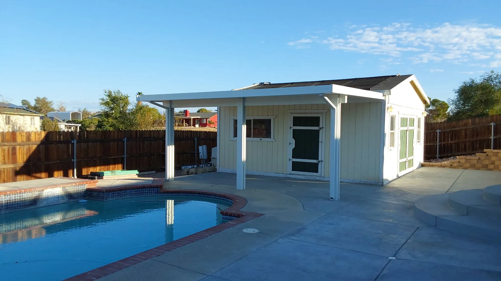 Patio cover extending along a pool house, framing the backyard pool