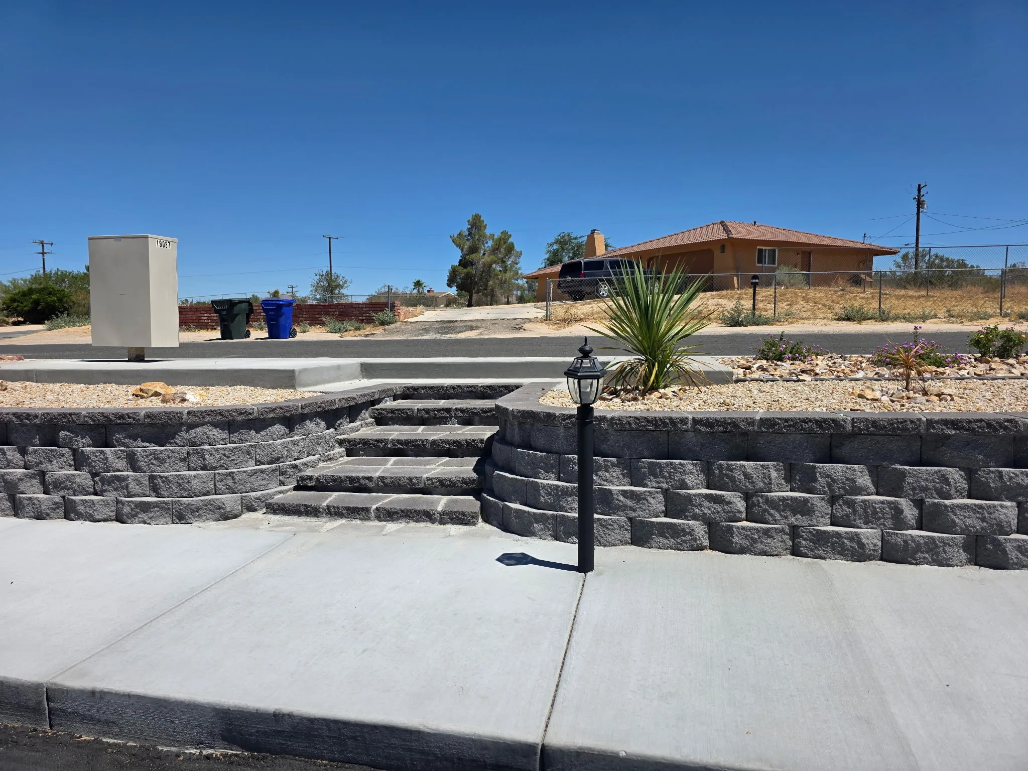 Curved segmental retaining wall with built-in steps and a lamp post along the street