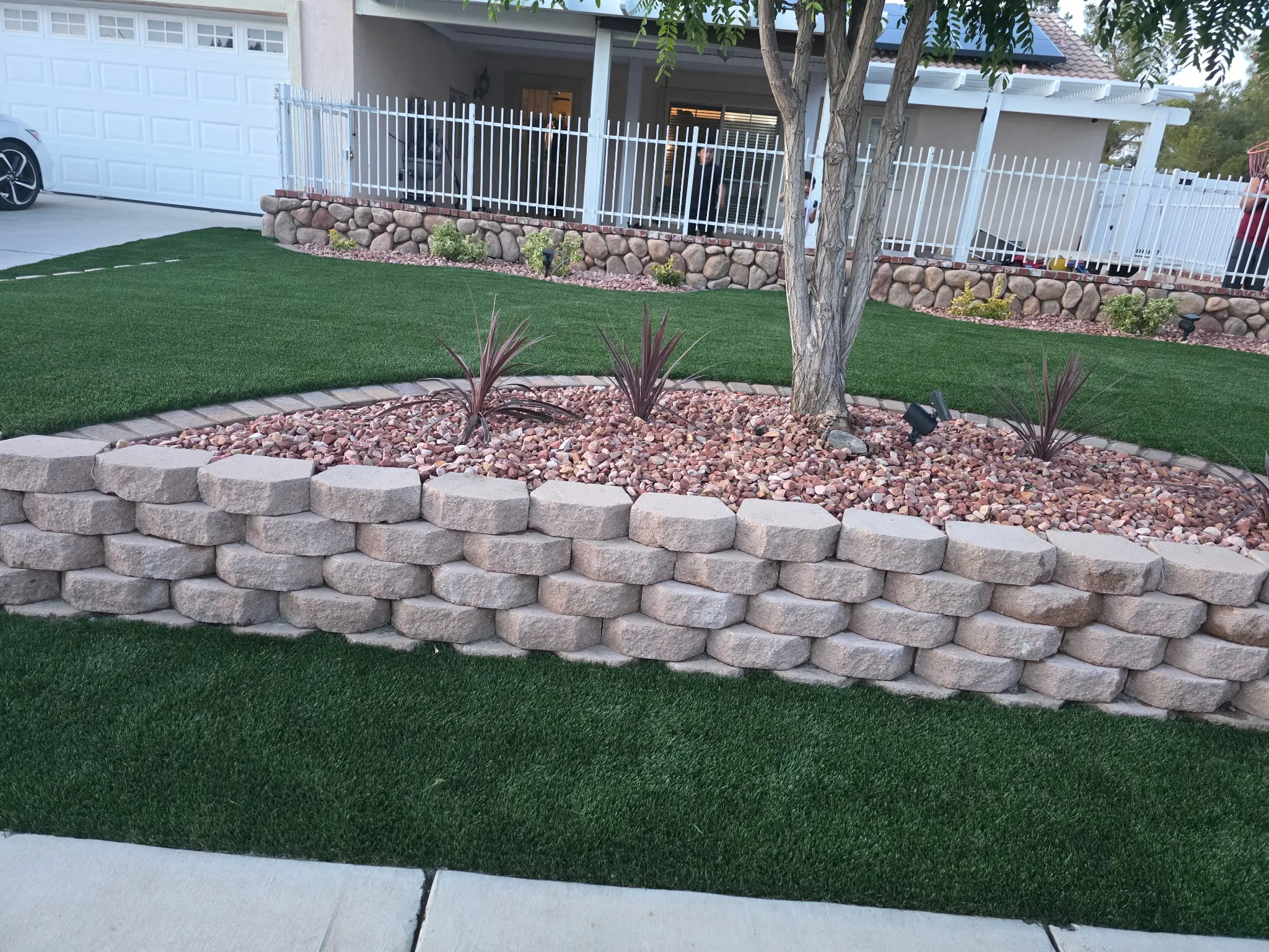 Tiered block planter surrounded by artificial grass and river rock